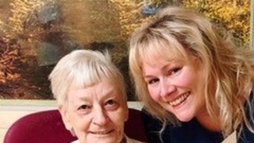 85er Geburtstag Kocar Die Jubilarin sitzt auf Stuhl und die Erste Beigeordnete beugt sich zu Ihr.