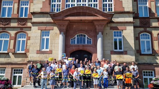 2vor12_Stadt_Friedrichsthal Stadtmitarbeiter stehen auf Rathaustreppe und schauen erbost. Schilder und Logos der Kampagne werden in die Luft gehoben.