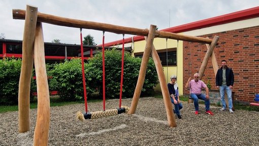 Frau und zwei Männer präsentieren die neue Kinderschaukel aus Holz