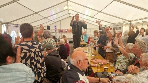 Der Sänger steht auf einer Bank im Festzelt, umgeben von feiernden Besuchern.