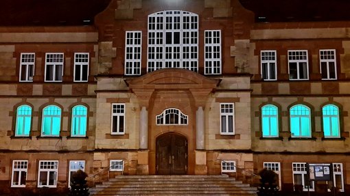 Fenster des Rathauses sind im Erdgeschoss grün beleuchtet, Blick vom Rathausvorplatz